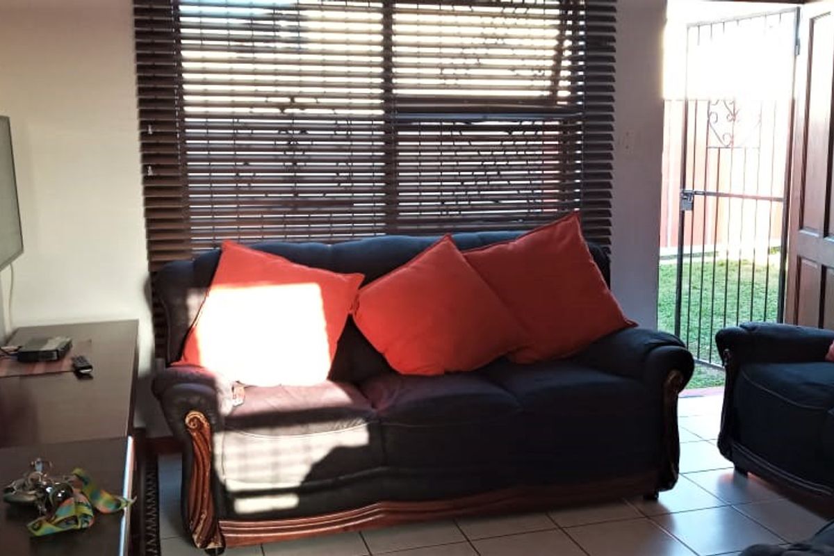 A living room featuring tiled flooring, venetian blinds, and direct access to the exterior through a security gate.