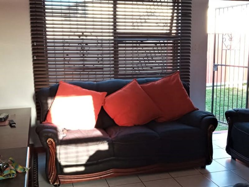 A living room featuring tiled flooring, venetian blinds, and direct access to the exterior through a security gate.