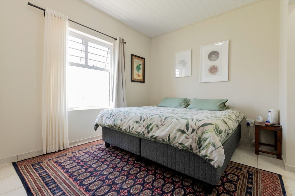 A well-maintained bedroom featuring tiled flooring, a timber panelled ceiling, and a window fitted with security bars.