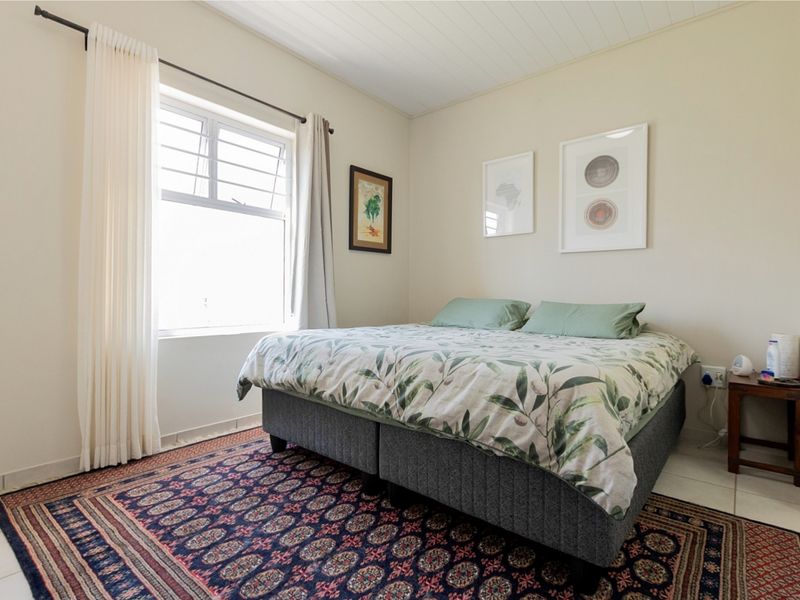 A well-maintained bedroom featuring tiled flooring, a timber panelled ceiling, and a window fitted with security bars.
