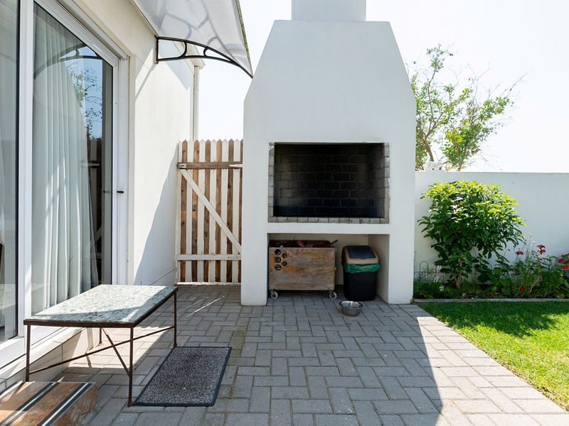 Outdoor patio area featuring a built-in braai, paved flooring, and direct access to the interior through sliding glass doors.