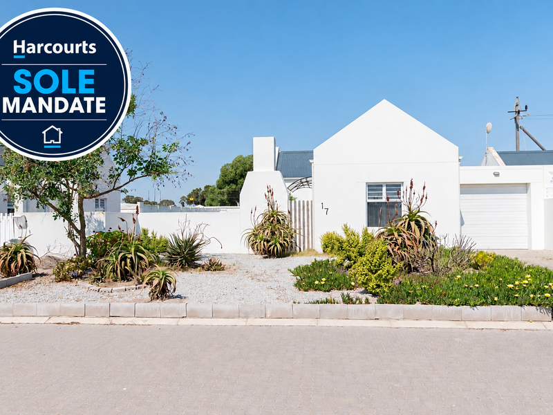 Front elevation of a single-story residence featuring a white facade, paved driveway, attached garage, and low-maintenance landscaped garden.