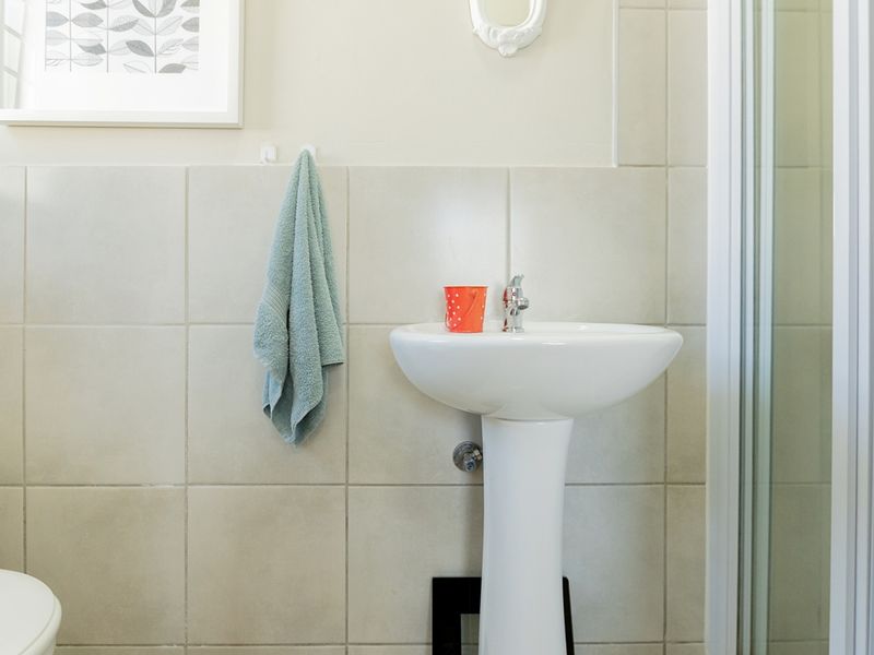 A functional bathroom featuring a white pedestal basin with chrome faucet and neutral ceramic wall tiling.