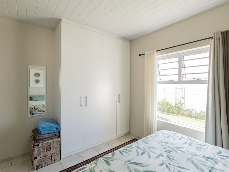 A bright bedroom featuring built-in wardrobes, tiled flooring, and a tongue and groove ceiling, offering a clean and functional living space.