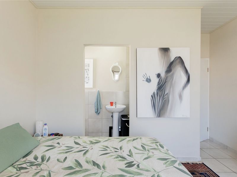 Bedroom featuring neutral walls, tiled flooring, and an adjoining en-suite bathroom with a pedestal basin.
