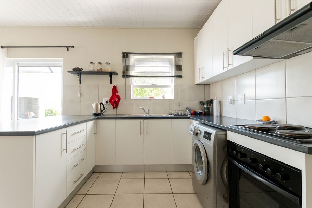 A functional kitchen featuring white cabinetry, dark countertops, tiled backsplash, and integrated appliances, with direct access to an outdoor area.