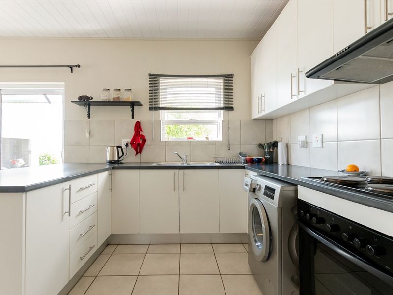 A functional kitchen featuring white cabinetry, dark countertops, tiled backsplash, and integrated appliances, with direct access to an outdoor area.