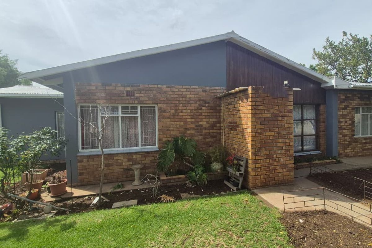 Rear view of the house featuring a combination of brick and timber cladding, metal roofing, and a surrounding garden area with concrete pathways.