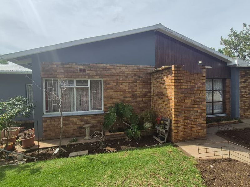 Rear view of the house featuring a combination of brick and timber cladding, metal roofing, and a surrounding garden area with concrete pathways.