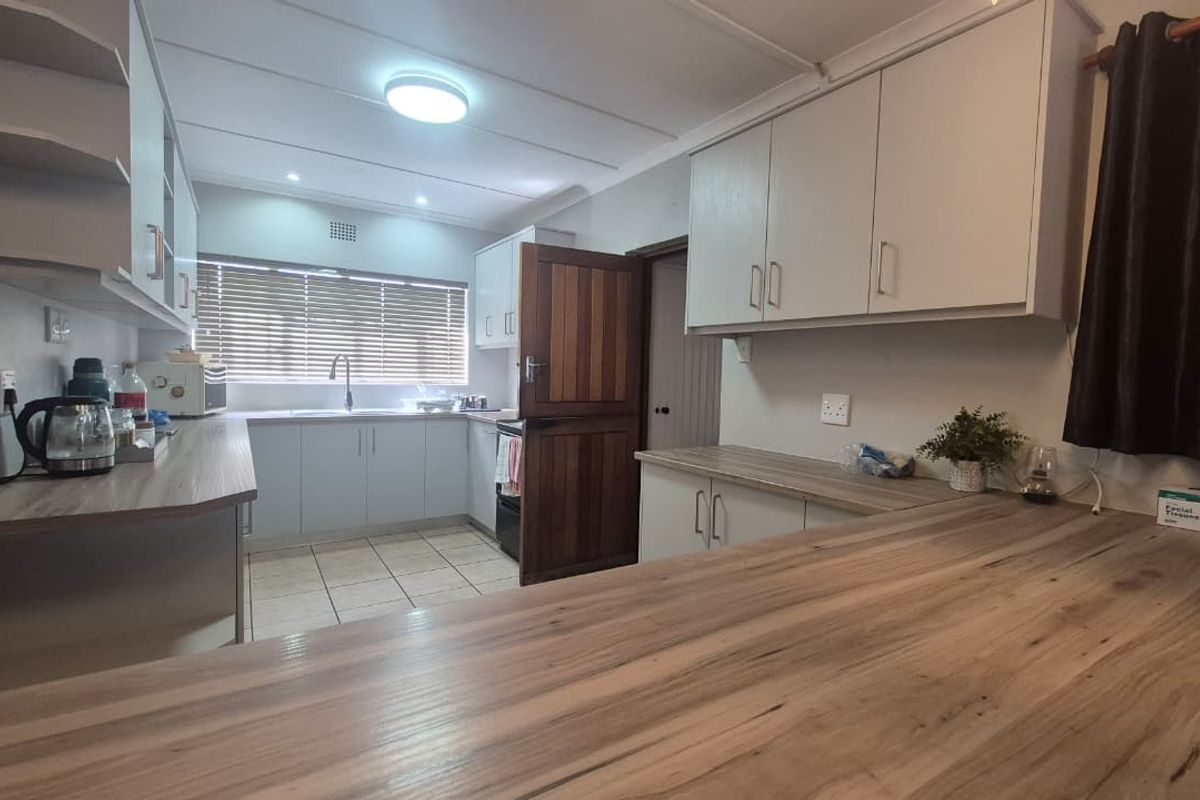 A functional kitchen featuring light-toned cabinetry, wood-look laminate countertops, tiled flooring, and a traditional stable door leading to the exterior.