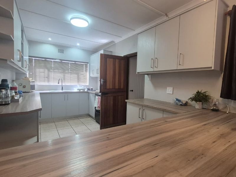 A functional kitchen featuring light-toned cabinetry, wood-look laminate countertops, tiled flooring, and a traditional stable door leading to the exterior.