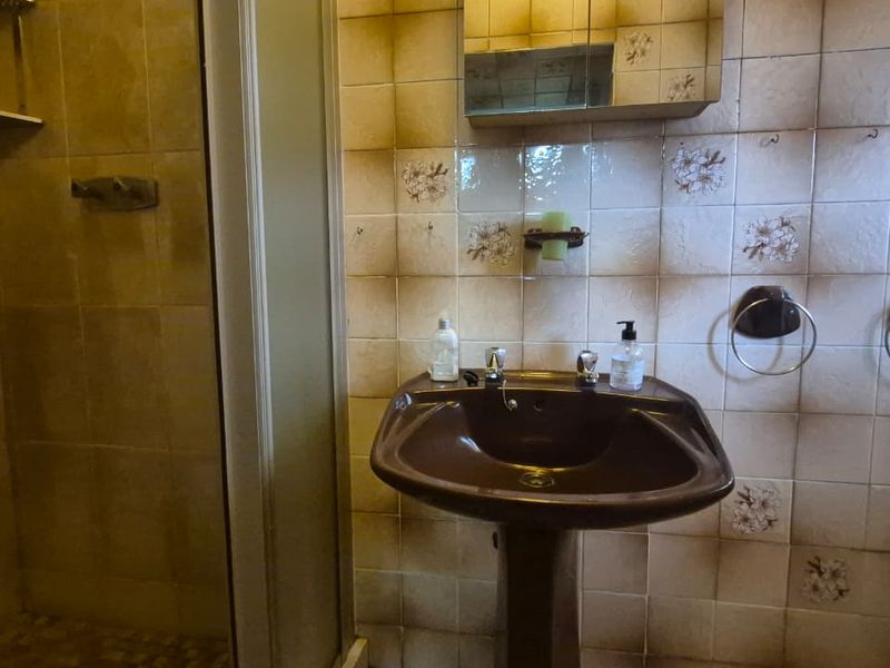 A dated bathroom featuring a pedestal sink, shower enclosure, and original wall tiling, offering significant potential for a modern renovation.