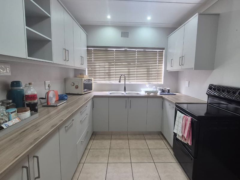 A functional kitchen featuring light-toned cabinetry, laminate countertops, a double basin sink, and tiled flooring, offering a clean and practical workspace.