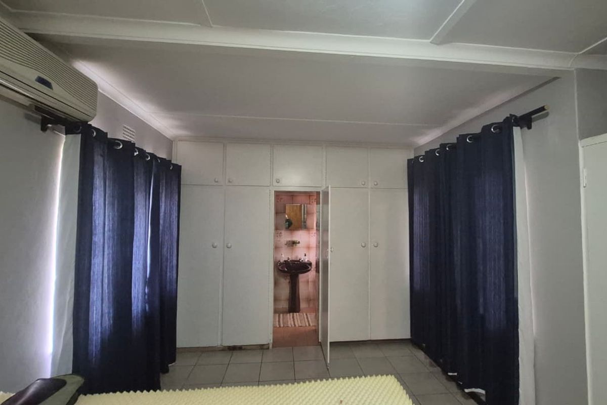 Bedroom featuring extensive built-in cupboards, tiled flooring, an integrated air conditioning unit, and direct access to an en-suite bathroom.