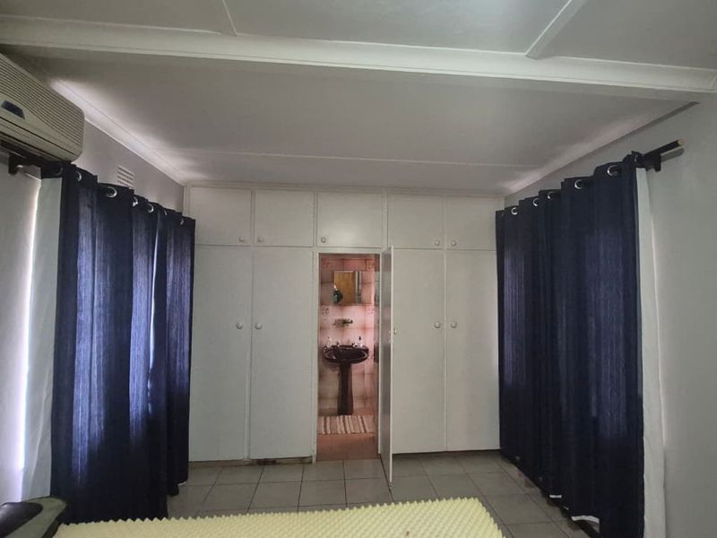 Bedroom featuring extensive built-in cupboards, tiled flooring, an integrated air conditioning unit, and direct access to an en-suite bathroom.