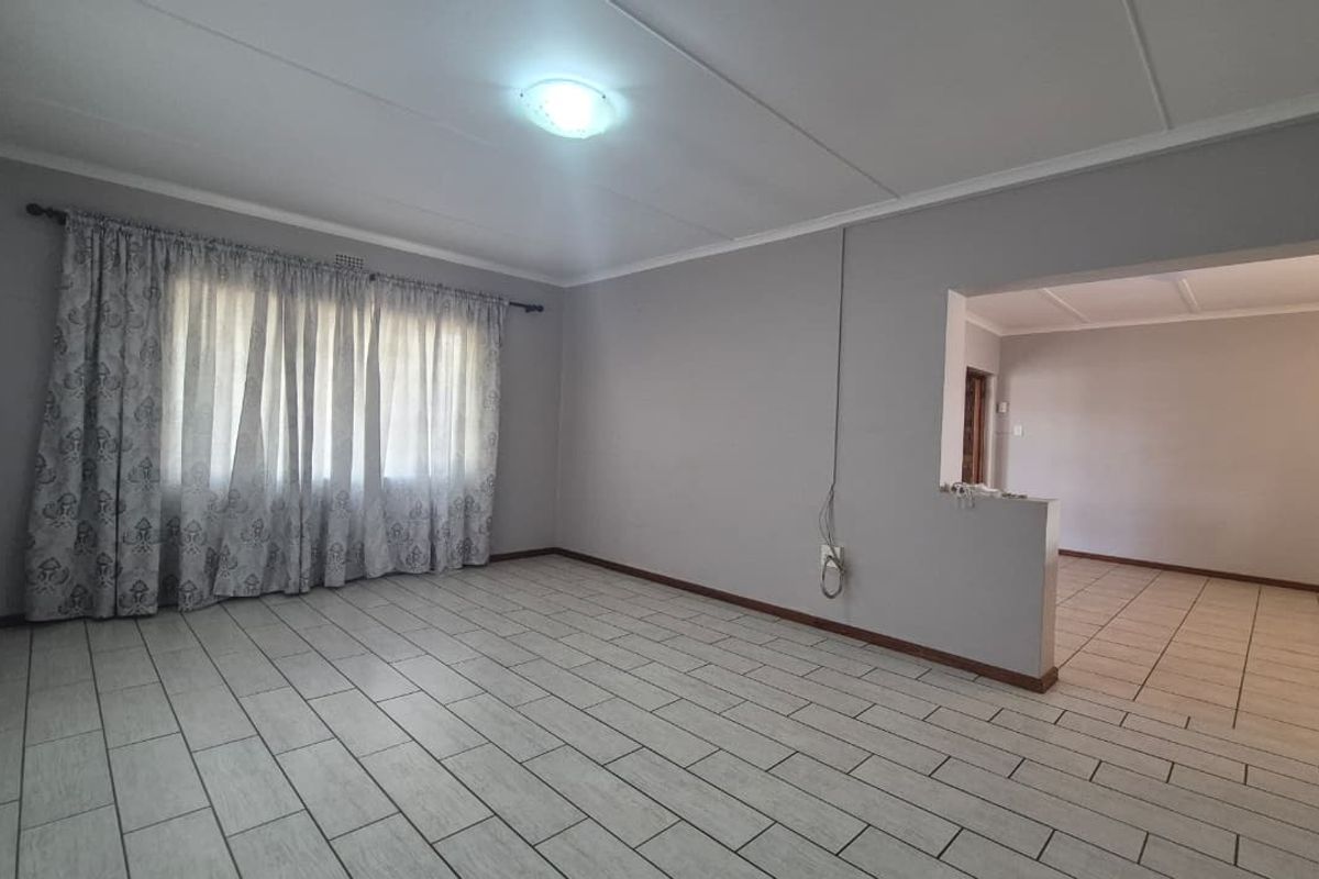 An empty, open-plan living area featuring neutral wall tones, tiled flooring, and a partition wall leading to an adjacent space.