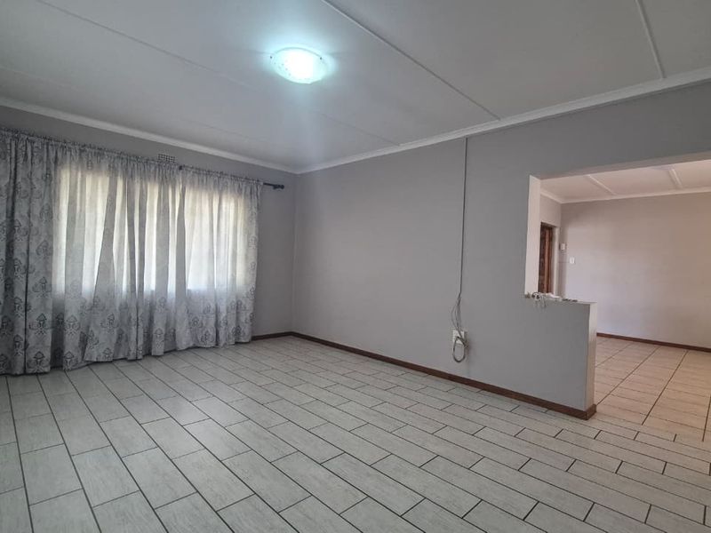 An empty, open-plan living area featuring neutral wall tones, tiled flooring, and a partition wall leading to an adjacent space.