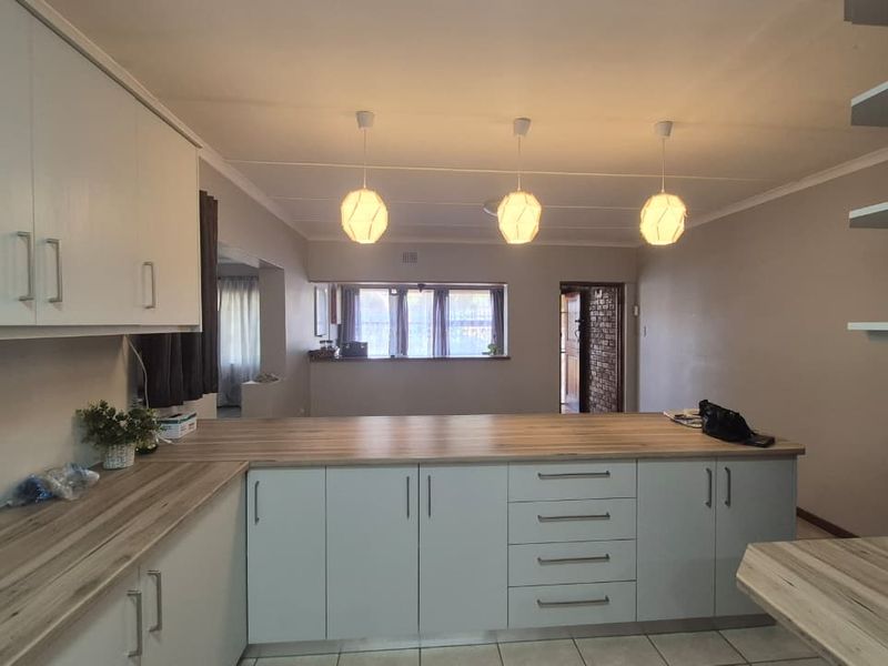 Modernized kitchen featuring light-toned cabinetry, wood-look laminate countertops, and a breakfast bar, illuminated by three contemporary pendant lights.