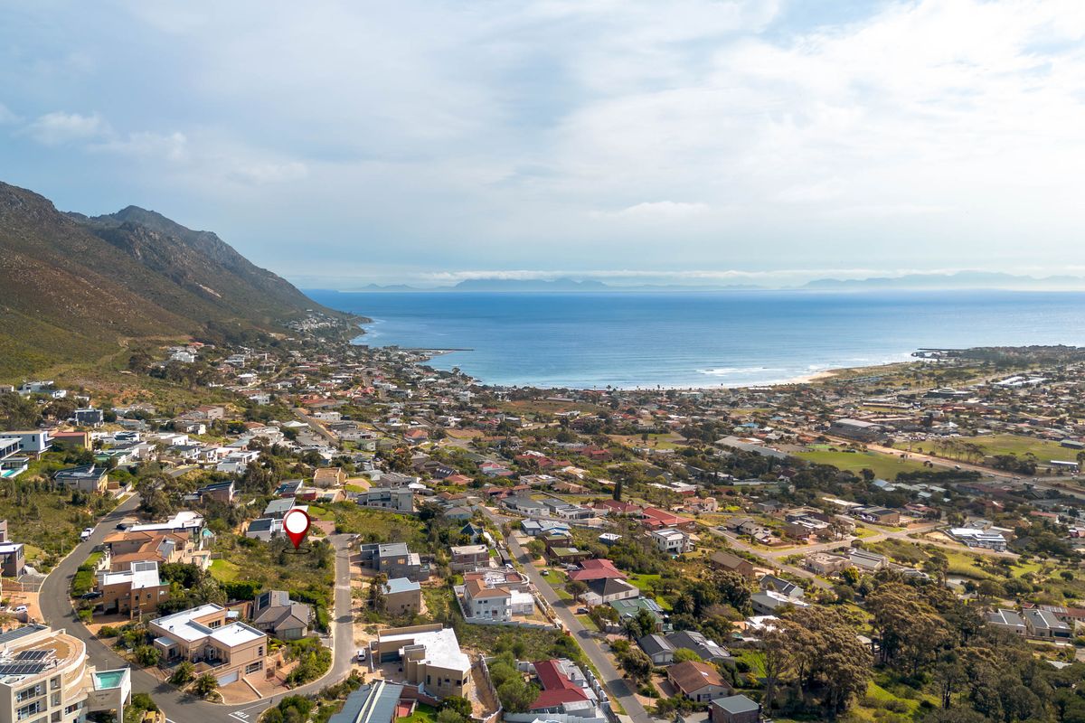 An aerial view of a vacant residential plot situated in a coastal neighborhood with scenic ocean and mountain views.
