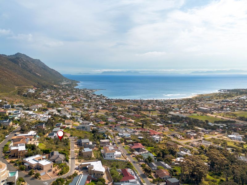An aerial view of a vacant residential plot situated in a coastal neighborhood with scenic ocean and mountain views.