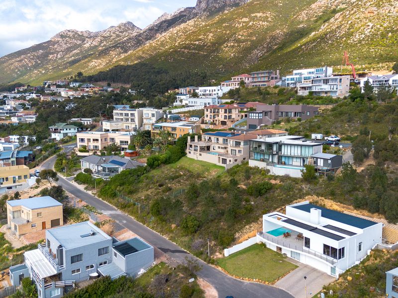 An aerial view of a residential hillside neighborhood featuring modern homes, paved streets, and scenic mountain backdrop.