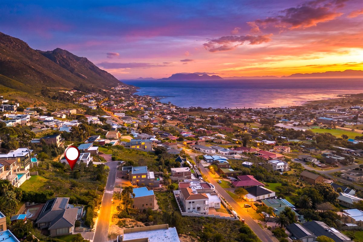 An elevated aerial view of a residential neighborhood at sunset, showcasing the coastal landscape, mountain backdrop, and surrounding community infrastructure.