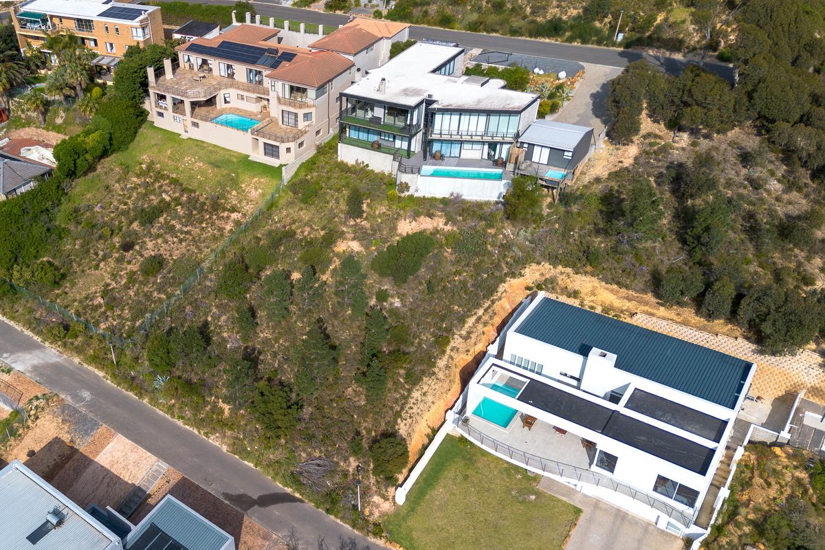 Aerial view of a residential hillside area featuring multiple modern homes with swimming pools, sloped landscaping, and surrounding road infrastructure.