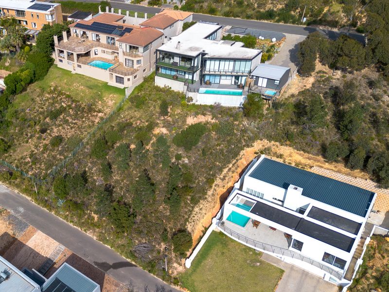 Aerial view of a residential hillside area featuring multiple modern homes with swimming pools, sloped landscaping, and surrounding road infrastructure.