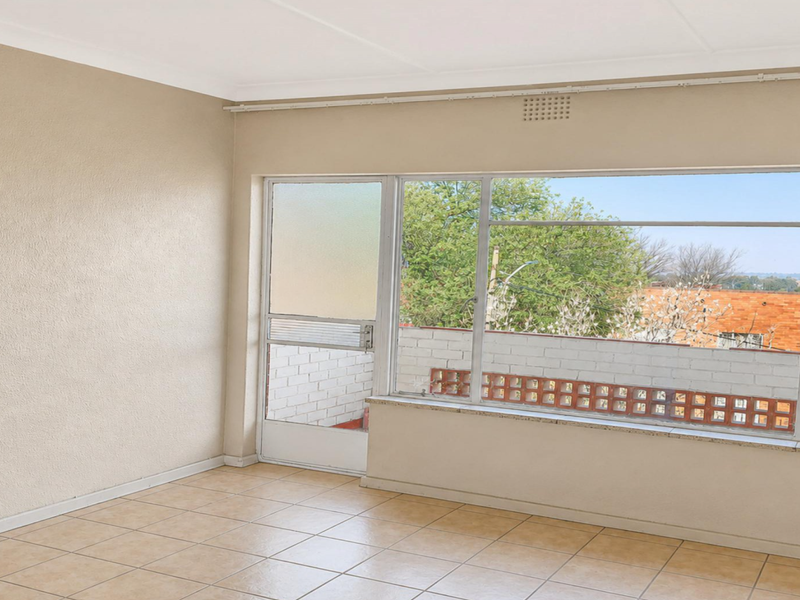 An empty living room featuring tiled flooring, coved ceilings, and large windows providing natural light and access to an outdoor balcony area.