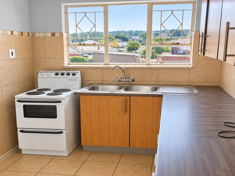 A functional kitchen featuring a freestanding stove, double basin sink, laminate countertops, and tiled splashbacks with a view through the window.