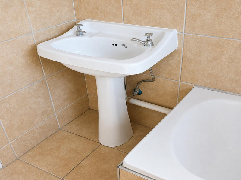 A functional bathroom featuring a white pedestal basin and bathtub with neutral ceramic wall and floor tiling.