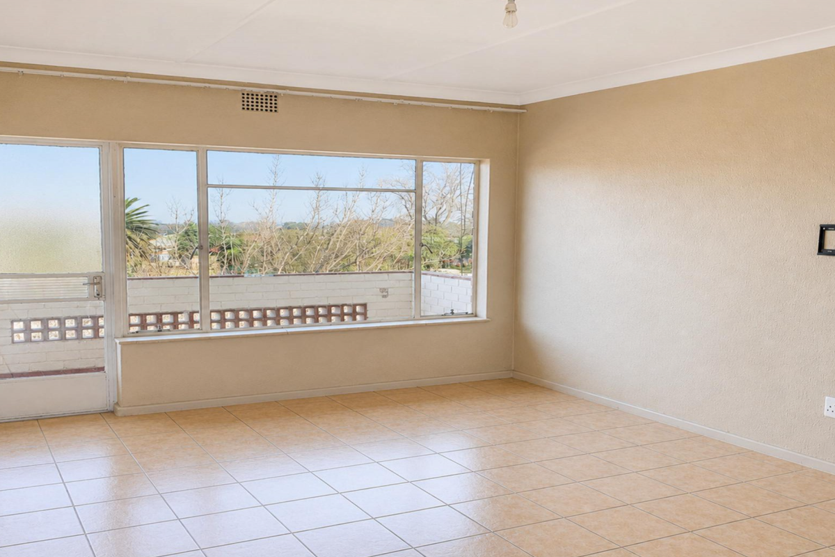 A bright, empty living room featuring tiled flooring, a large window with natural light, and direct access to an outdoor balcony area.