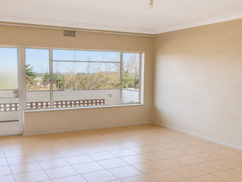 A bright, empty living room featuring tiled flooring, a large window with natural light, and direct access to an outdoor balcony area.
