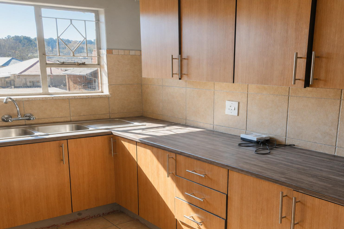 A functional kitchen featuring wood-look laminate cabinetry, dark laminate countertops, a double basin sink, and neutral ceramic wall tiling.