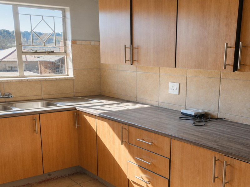 A functional kitchen featuring wood-look laminate cabinetry, dark laminate countertops, a double basin sink, and neutral ceramic wall tiling.