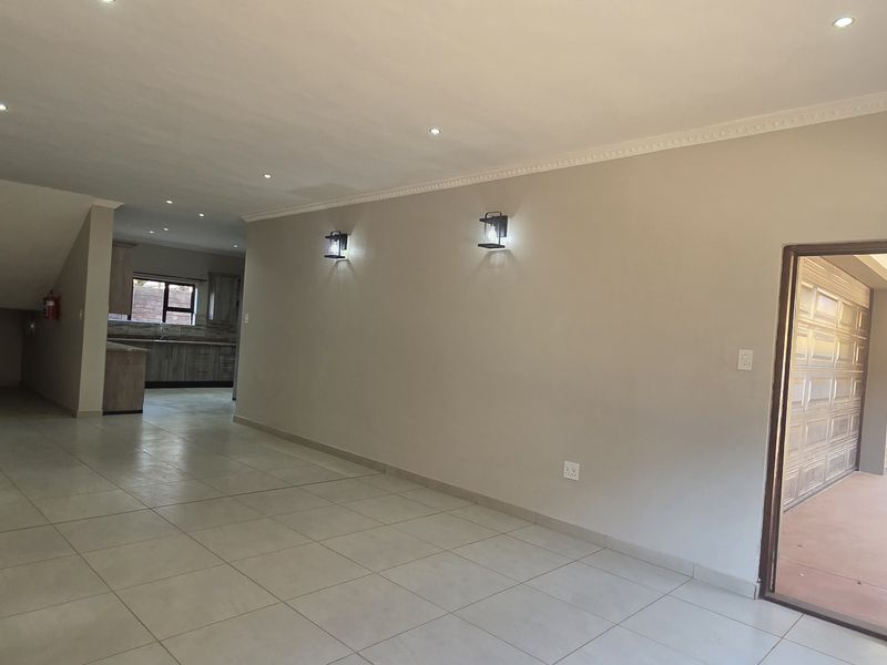 Spacious open-plan living area featuring tiled floors, recessed lighting, and a staircase, leading into a kitchen space with built-in cabinetry.