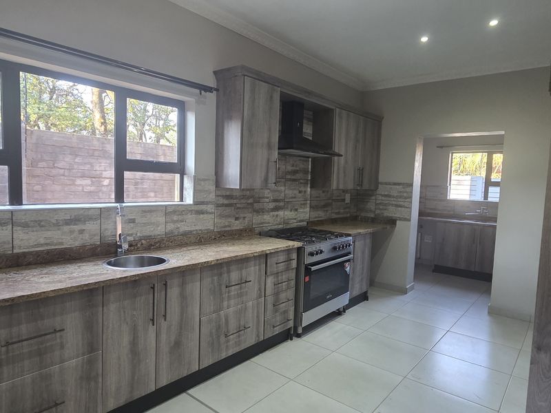 Modern kitchen featuring wood-grain cabinetry, stone countertops, gas stove, and a separate scullery area with tiled flooring and ample natural light.