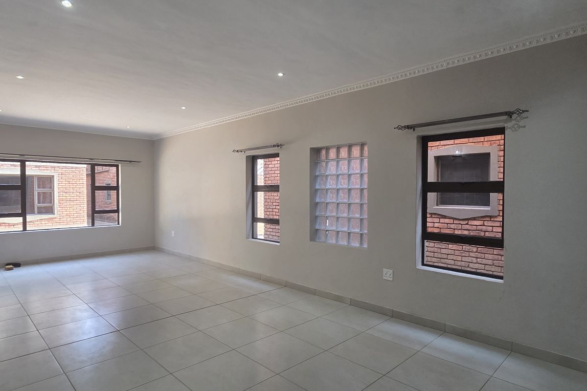 Spacious, empty living area featuring neutral tiled flooring, recessed downlights, and a combination of aluminium and glass block windows.