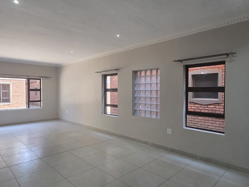 Spacious, empty living area featuring neutral tiled flooring, recessed downlights, and a combination of aluminium and glass block windows.