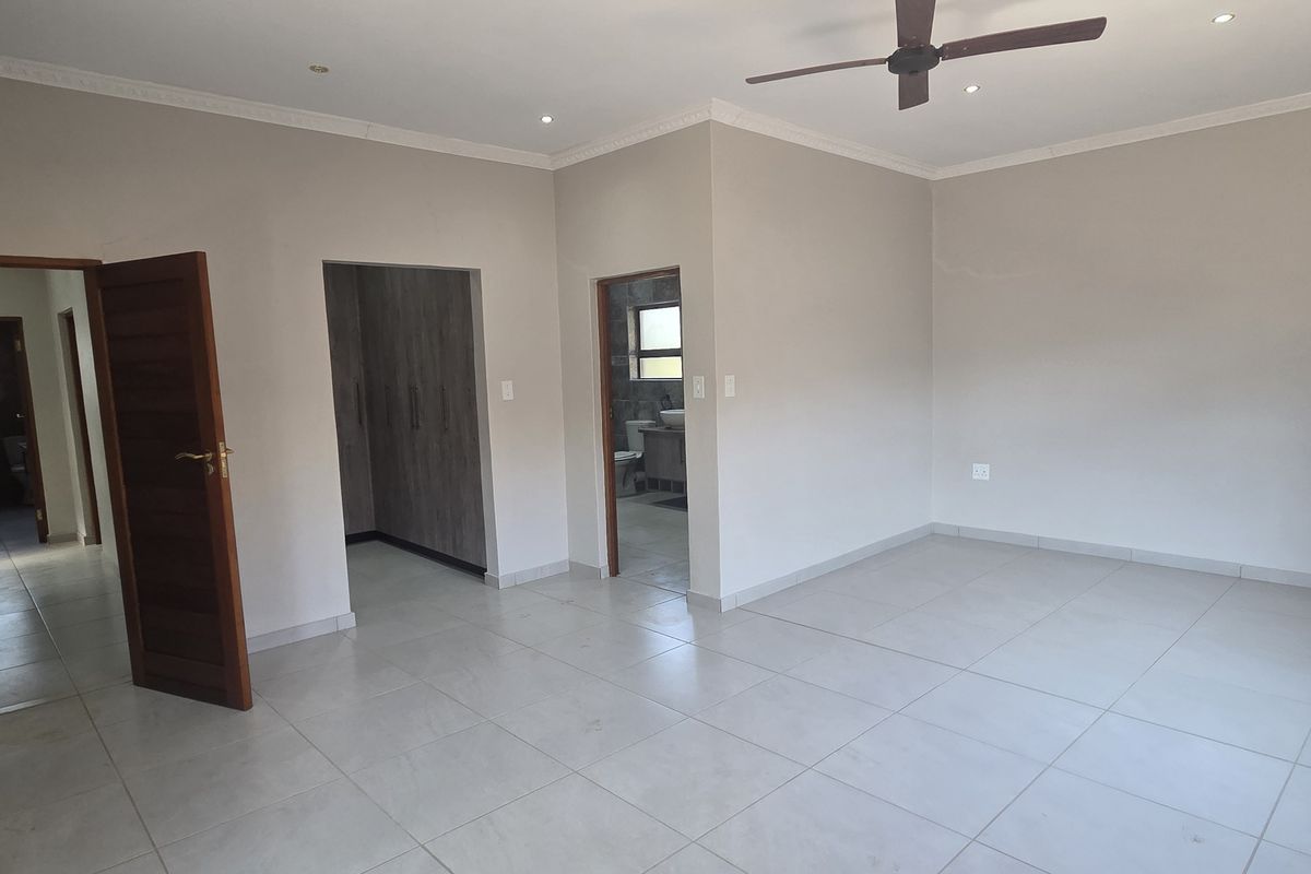 Spacious bedroom featuring neutral tiled flooring, built-in cupboards, recessed downlights, and a ceiling fan, offering a clean and well-maintained living space.