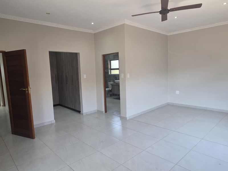 Spacious bedroom featuring neutral tiled flooring, built-in cupboards, recessed downlights, and a ceiling fan, offering a clean and well-maintained living space.