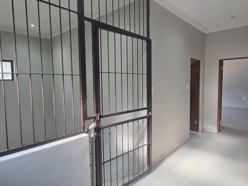 A clean, tiled hallway featuring a secure metal gate, recessed lighting, and neutral wall finishes leading to adjacent rooms.