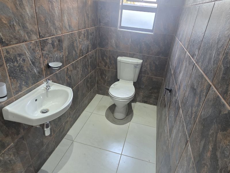 A compact guest bathroom featuring full-height dark stone-look wall tiles, a white floor, a wall-mounted basin, and a standard toilet.
