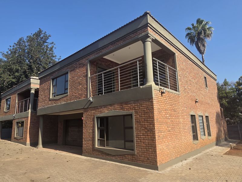 A double-story face brick townhouse featuring a paved driveway, integrated garage, and an upper-level balcony with stainless steel balustrades.