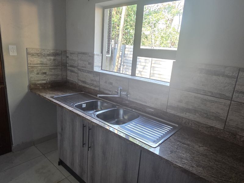 A clean and functional scullery area featuring a double stainless steel sink, granite countertops, and modern tiled splashbacks.