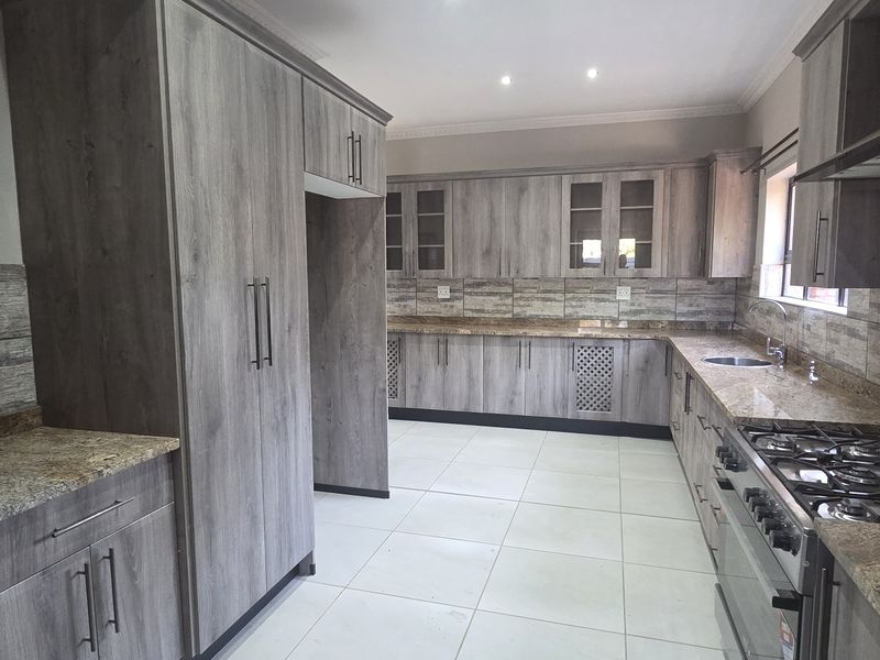 Modern kitchen featuring extensive wood-grain cabinetry, granite countertops, a gas hob with extractor, and neutral tiled flooring in a spacious, clean layout.