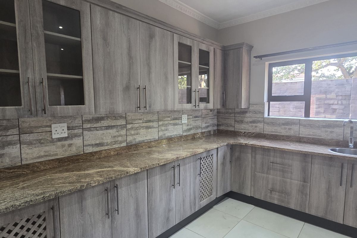 Modern kitchen featuring grey wood-look cabinetry, granite countertops, tiled backsplash, and large windows providing natural light.