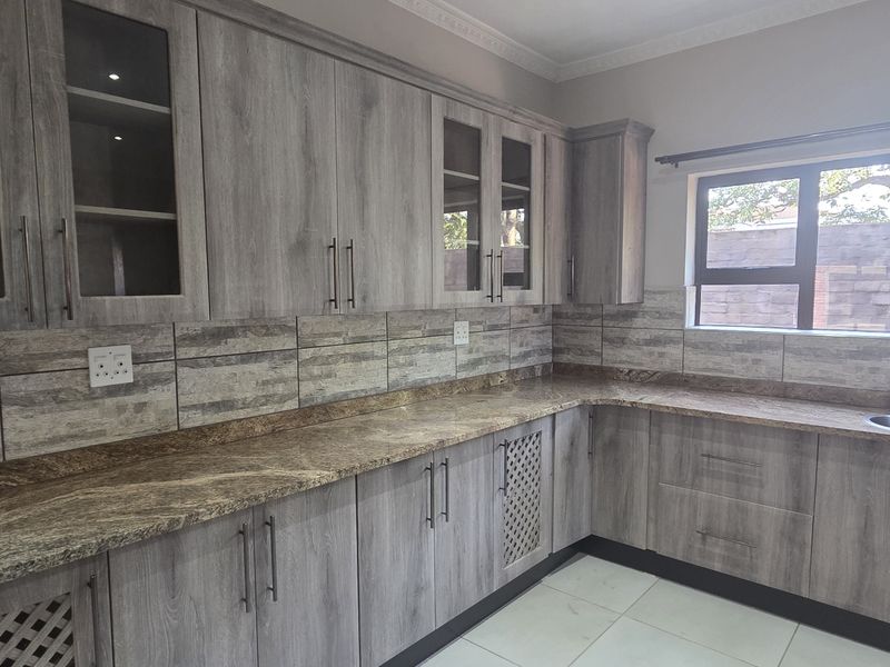 Modern kitchen featuring grey wood-look cabinetry, granite countertops, tiled backsplash, and large windows providing natural light.