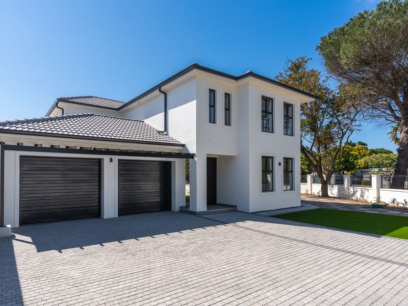 Modern double-storey residential home featuring a paved driveway, double garage with black roller doors, and a well-maintained front garden area.