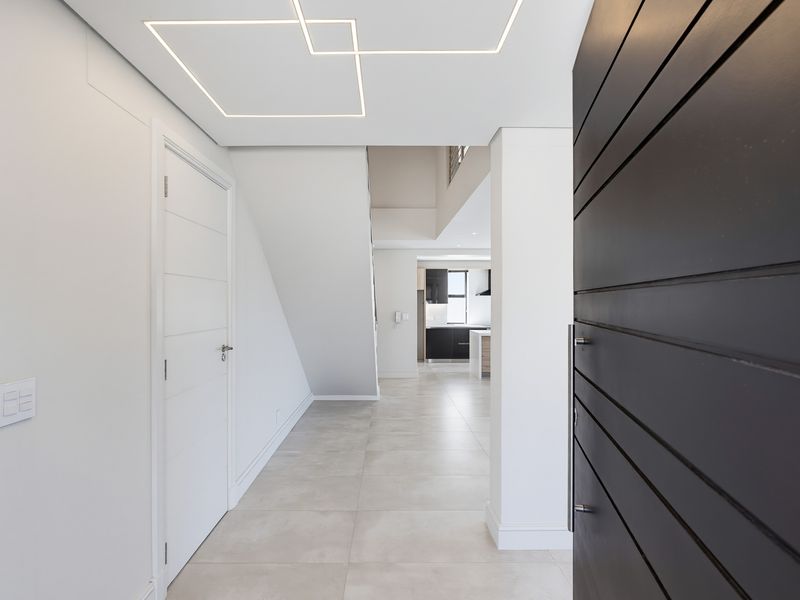 Modern entrance hall featuring clean lines, large format floor tiles, recessed geometric ceiling lighting, and a contemporary pivot front door.